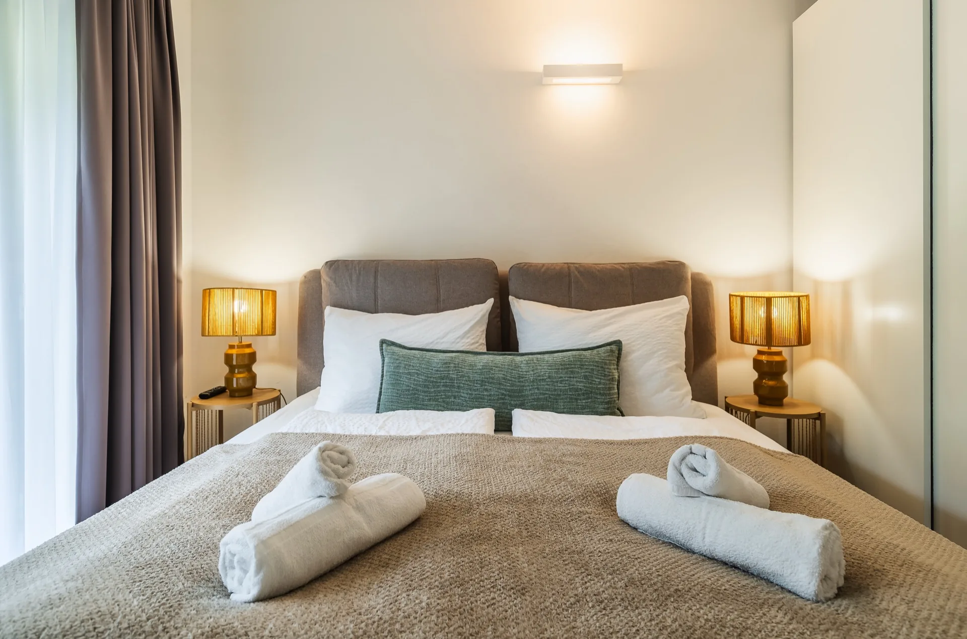 Elegantes Schlafzimmer mit Boxspringbett, goldenen Nachttischlampen, weißer Bettwäsche und gerollten Handtüchern im Alpstay Chalet Nr.2 Bad Kleinkirchheim – Schlafzimmerfotografie Ferienwohnung Kärnten