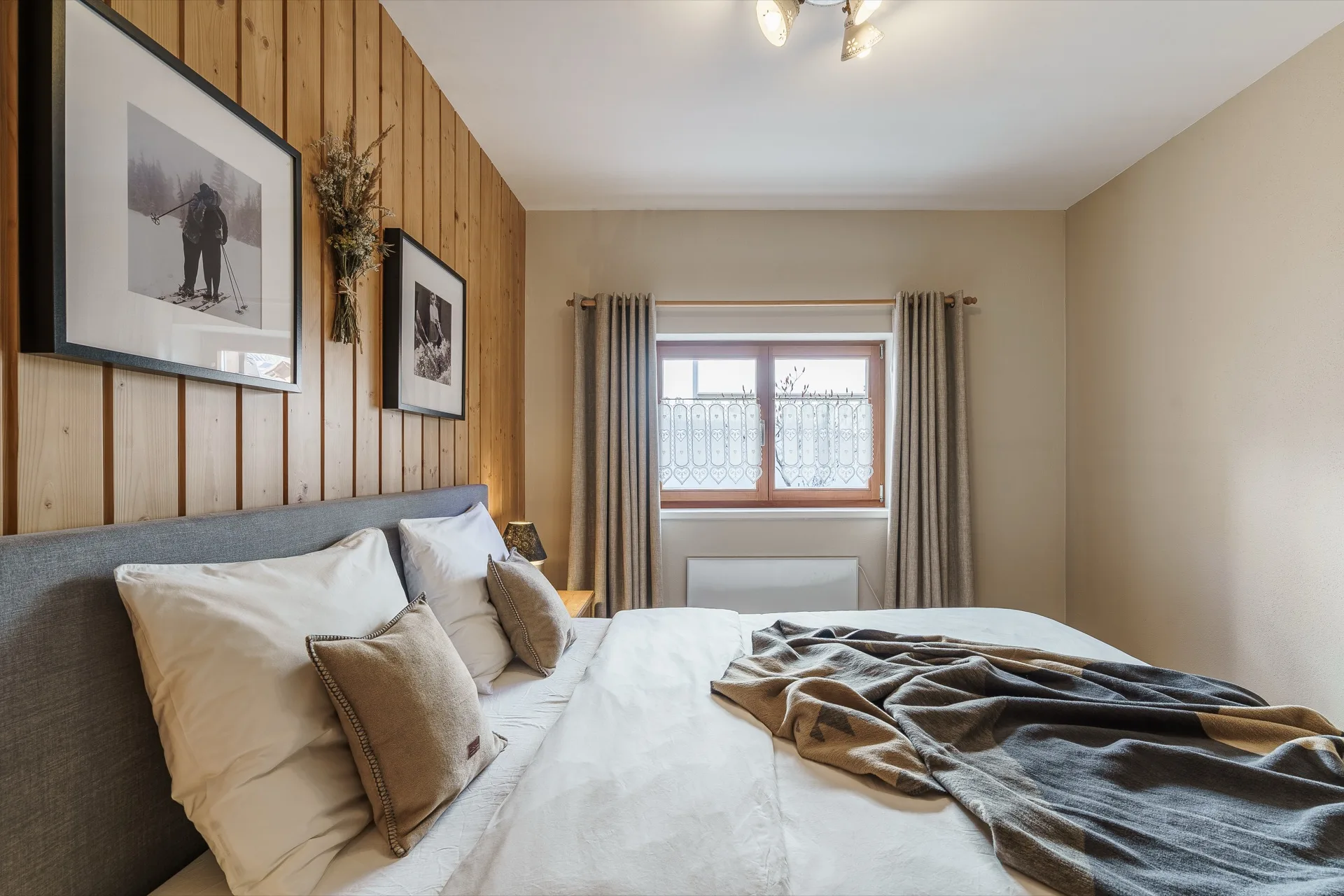 Helles Schlafzimmer mit Holzwandverkleidung, weißer Bettwäsche und Vintage-Ski-Wandfotos in der Ferienwohnung Holländer Kärnten – alpine Schlafzimmerfotografie