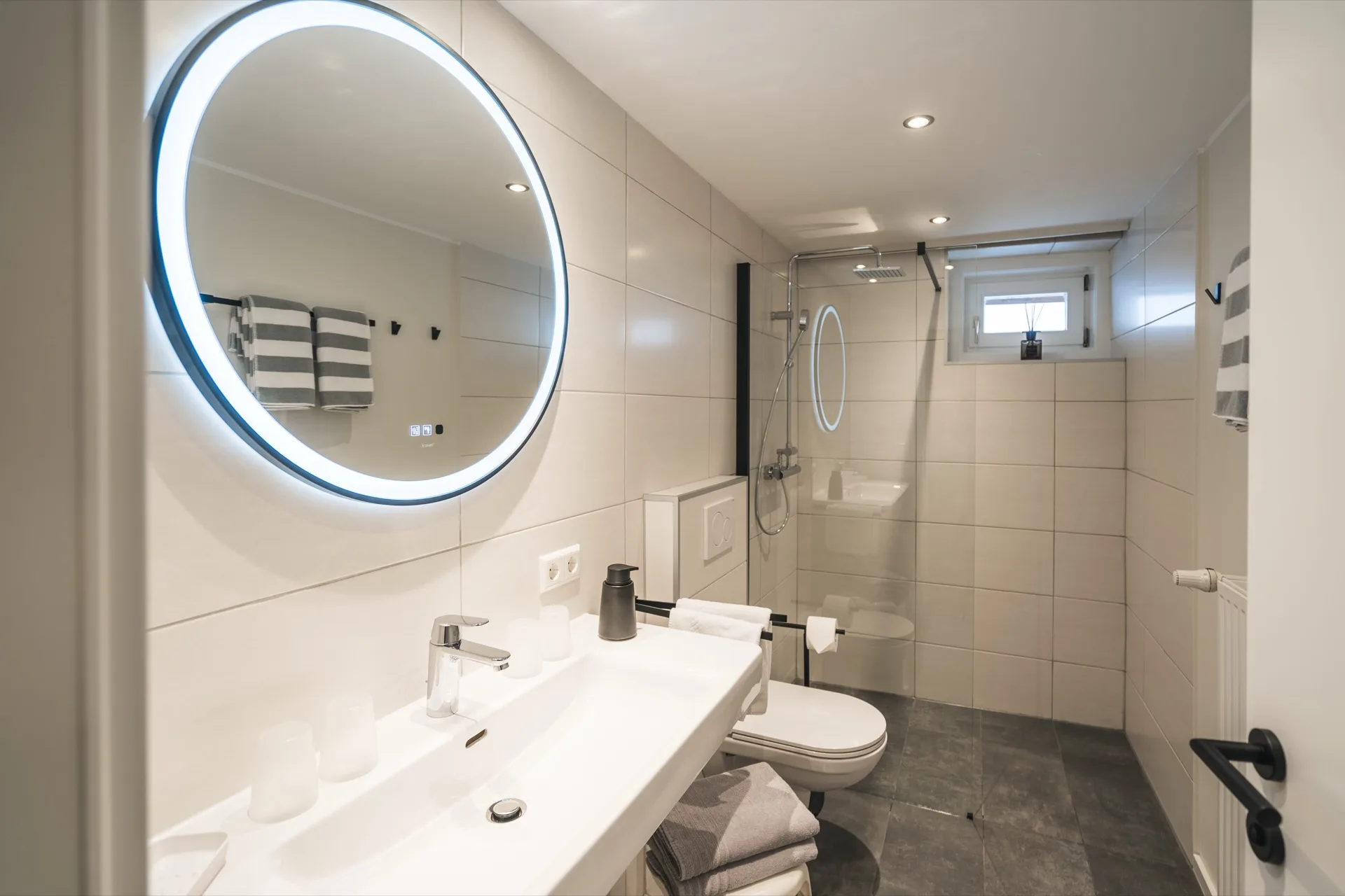 Modernes Badezimmer mit rundem LED-Spiegel, ebenerdiger Dusche und hochwertiger Ausstattung im Landhaus Prägant Bad Kleinkirchheim – Ferienwohnung Fotografie Kärnten